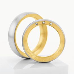 Zwei Eheringe aus Gold und Silber, ein Ring mit drei Diamanten und Gravur im Inneren.