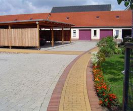 Gepflasterter Hof mit Blumenbeet, Garage und überdachtem Carport an einem Wohnhaus.