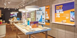 Telefoonwinkel interieur met uitgestalde smartphones en feloranje promotieposters aan de muur.