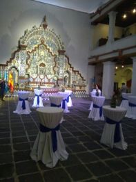 Mesas altas con manteles blancos en un salón decorado con mosaicos, ambiente de evento elegante.