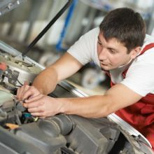 Mechanic in red overalls working on a car engine in a garage.