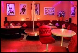 Gemütliche Lounge mit rotem Licht, runden Tischen, Sesseln und Fotos an rosa Wänden.