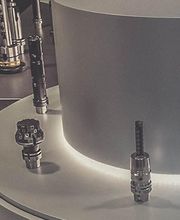 Mehrere metallische Geräte auf einer runden, beleuchteten Ausstellungsfläche in einem Raum.