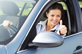 Frau im Auto zeigt Daumen hoch und lächelt aus dem offenen Fenster.