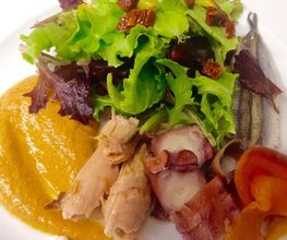 Ensalada gourmet con lechuga, puré, pescado y mariscos en un plato blanco.
