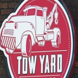 Red and white "Tow Yard" sign with illustration of a tow truck.