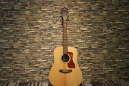 Akustikgitarre vor einer rustikalen Steinwand platziert.