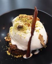 Postre de helado sobre brownie, decorado con nueces y caramelo en un plato negro.