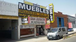 Fachada de tienda de muebles con carteles de liquidación y una furgoneta afuera.
