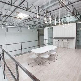Bright loft space with a white table, chairs, and hanging lights in a modern industrial setting.