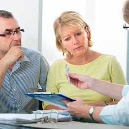Three people in a meeting, reviewing documents and holding pens.