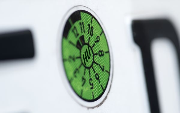 Eine grüne TÜV-Plakette auf einem Nummernschild eines PKWs, in Nahaufnahmen.