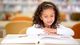 Young girl reading a book at a table in a library setting.