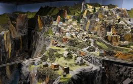 Miniature mountainous landscape with model houses and roads on rugged terrain.