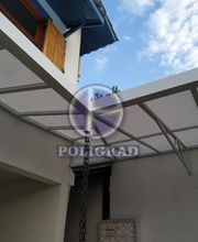 Pátio com cobertura de estrutura metálica e vidro, parede branca e céu azul ao fundo.