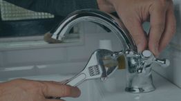 Hands fixing a chrome faucet with a wrench in a bathroom setting.