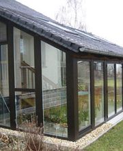 Moderner Wintergarten mit Glaswänden und schwarzem Rahmen, angrenzend an ein Haus im Garten.