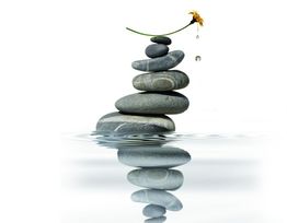 Stein-Stapel im Wasser mit Blume und Wassertropfen, die Ruhe und Balance symbolisieren.