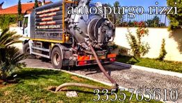 Camion di autospurgo in azione in un giardino con numero di contatto visibile.