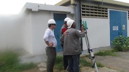 Três pessoas com capacetes operam um equipamento de medição em um local industrial.