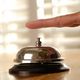 Finger pressing a silver service bell on a wooden surface with a blurred background.
