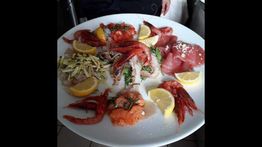 Piatto di pesce crudo con gamberi rossi, fettine di limone e verdure su un grande piatto bianco.