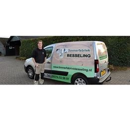 Man naast bedrijfswagen van Timmerfabriek Besseling, geparkeerd op een erf.