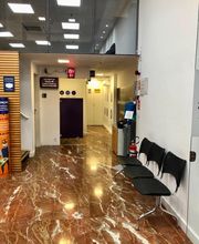 Corredor com piso de mármore, cadeiras pretas e sinal de senha eletrônica.