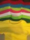 Seis camisetas de colores: rojo, azul, amarillo, rosa, verde y blanco, apiladas ordenadamente.