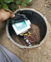 Dispositivo electrónico en caja circular en la tierra, con cables y mano visible.