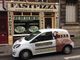 Voiture de livraison "FastPizza" garée devant la pizzeria, avec enseigne et numéro de téléphone.