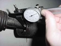 Dial caliper measuring pipe diameter, held by a hand.