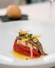 Plato gourmet de pimiento rojo asado con anchoa y acompañamientos, presentado en un plato blanco.