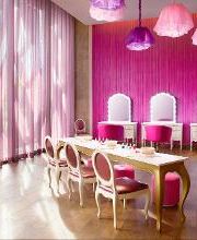 Sala de belleza rosa con cortinas, tocadores, sillas elegantes y lámparas de techo coloridas.