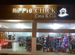 Fachada da loja "Hippie Chick Casa & Cia" iluminada com decoração de Natal e árvores enfeitadas.