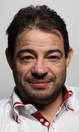 Homme souriant avec une chemise blanche et rouge, regardant vers l'avant.