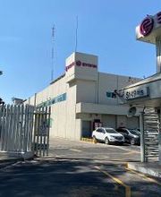 Edificio blanco con logos de empresa y estacionamiento, visto desde el portón de entrada.