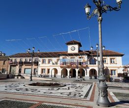 Plaza con farolas, edificio con reloj y cielo azul.