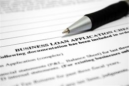 A pen rests on a business loan application form with text visible.