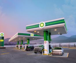 Estación de servicio con tres coches, montañas al fondo y un cielo colorido al atardecer.