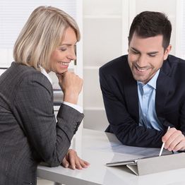 Two professionals smiling and looking at a tablet together in an office setting.
