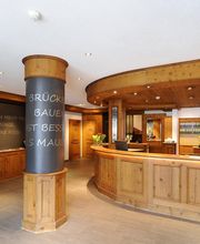 Holzgetäfelter Empfangsbereich eines Hotels mit Blumen und Schriftzug an der Säule.