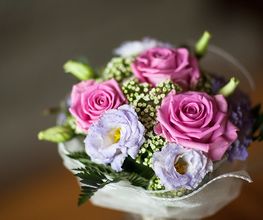 Bouquet di rose rosa e fiori lilla con foglie verdi sfondo sfocato.