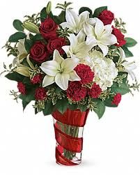 Bouquet of red roses, white lilies, and greenery in a red glass vase.