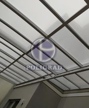 Cobertura de vidro com estrutura metálica em ambiente interno. Logo da Poligrad visível.