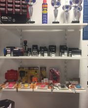 Regale mit Büromaterialien und Trophäen an einer Wand. Links sind Schlüsselanhänger zu sehen.