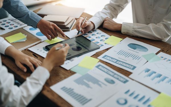 Mehrere Kollegen einer Firma sitzen zusammen vor verschiedenen Finanzdiagrammen um die Strategie der Unternehmensfinanzen zu optimieren.