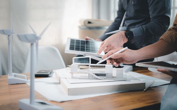 Zwei Ingenieure besprechen an einem Modell eines Bürogebäudes, wie sie die Energiewende des Unternehmens sinnvoll umsetzten können.