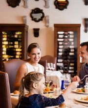 Familia cena en un restaurante elegante, con mesa llena de comida y vino. Ambiente acogedor.