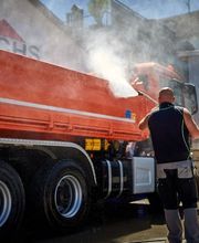 Mann reinigt roten Lkw mit Hochdruckreiniger im Freien neben Gebäude mit Fuchs-Logo.